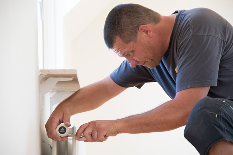 En ejendomsfunktionær tjekker termostaten på en radiator. || BM-Bytte bolig-JL-5356.jpg