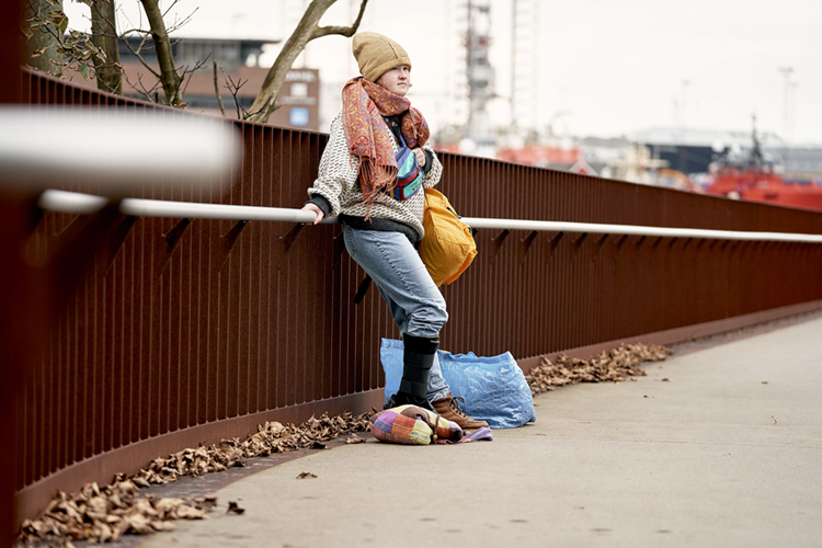 Billedet viser en ung pige, der står op af et rækværk med en gul rygsæk. En blå Ikea-pose er placeret ved siden af på jorden. || Foto Til PM Om Ungdomsboliger I Carlsberg Byen, Steffen Stamp 375 (1)