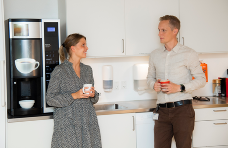 En kvinde og en mand står i køkkenet og taler med hver en kop kaffe i hånden. || Arbejdsplads Koekken