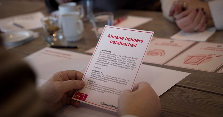 Et par hænder holder et målepunktskort fra AlmenKompas med overskriften 'Almene boligers betalbarhed' || Domea Almenkompas Prioriteringsworkshop