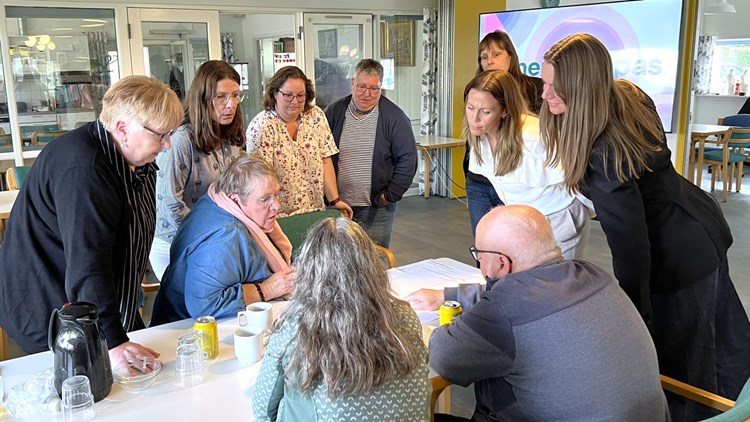 Gruppe på 10 personer står og sidder om et stort prioriteringsark på et bord. || Vendersbo Workshop 01 1600X900