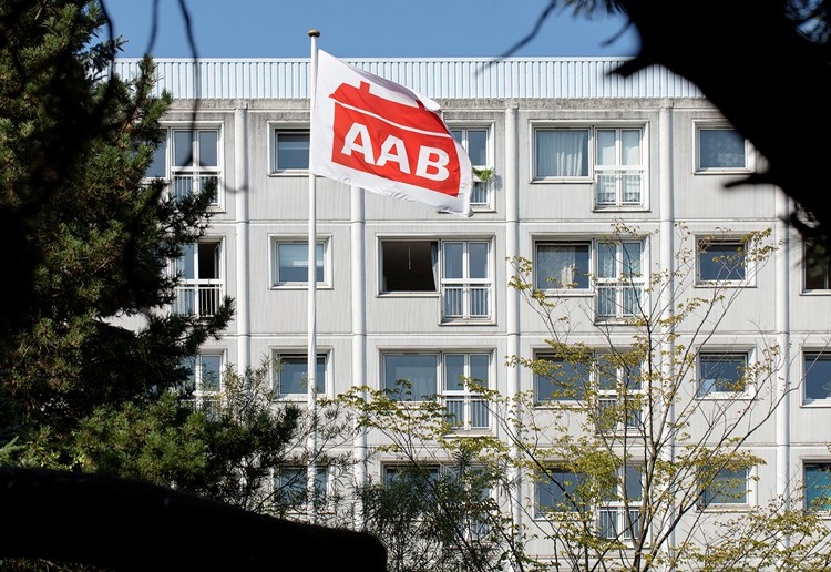 Flag med rødt AAB-logo vejer foran almen boligblok. || AAB Flag 1600X900